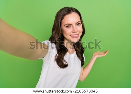 Photo of dreamy cute young lady wear white t-shirt recording self video showing arm empty space isolated green color background