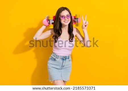 Photo of positive pretty lady hold skate hand finger demonstrate v-sign isolated on yellow color background