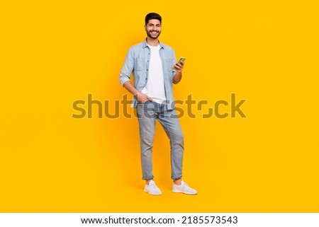 Full size photo of attractive hispanic guy hold gadget blogging write post wear stylish jeans outfit isolated on yellow color background Royalty-Free Stock Photo #2185573543