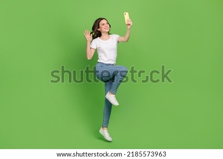 Photo of adorable sweet young lady wear white t-shirt jumping high video talk modern device isolated green color background