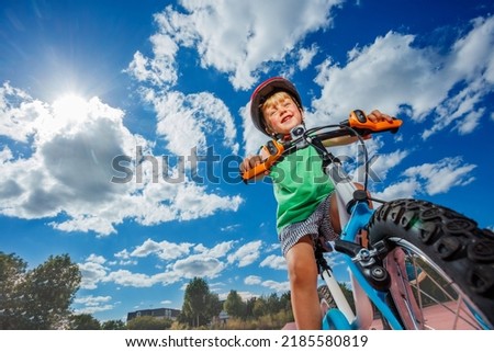Low angle photo of the boy on the little bicycle ride over sun and on background
