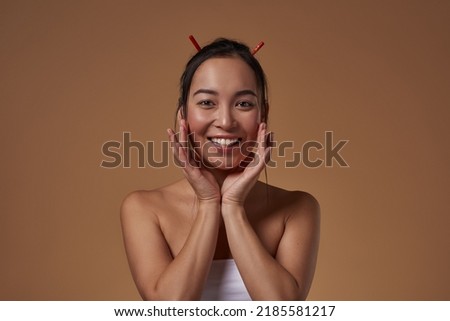 Portrait of smiling fashionable asian girl looking at camera. Pretty young brunette slim woman wearing tank top. Female beauty. Isolated on orange background. Studio shoot. Copy space