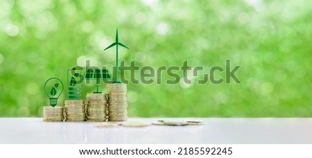 Renewable or clean energy generation prices and costs, financial concept : Green eco-friendly symbols atop coin stacks e.g. energy efficient light bulb, a battery, a solar cell panel,  a wind turbine. Royalty-Free Stock Photo #2185592245
