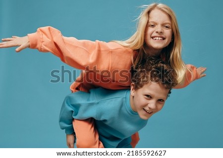 happy joyful children, brother and sister of school age play together and the boy rolls the girl on his back. Horizontal studio photography on a blue background
