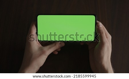 Man using phone with green screen on black wwalnut table , wide photo