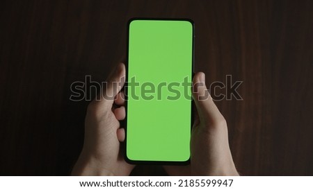 Man using phone with green screen on black wwalnut table , wide photo