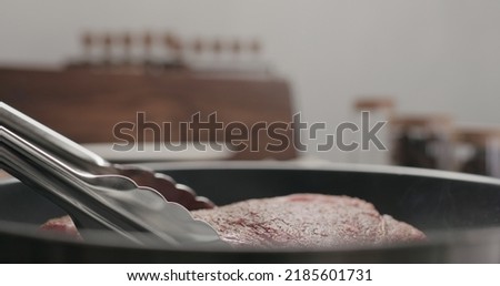 cooking new york steak on nonstick pan with tongs, wide photo