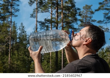 A person drinks water in nature from a large plastic bottle. Background picture.