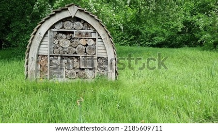 Large wooden purpose built inset house stood on grass near the field boundary and trees giving insects of all types somewhere to rest or lay their eggs. Royalty-Free Stock Photo #2185609711