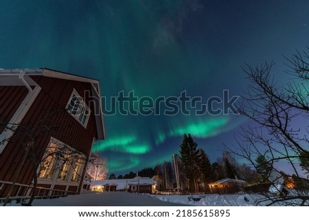 Fantastic winter landscape with wooden house with light in window in snowy mountains and Northern light in night sky. Christmas holiday and winter vacations concept
