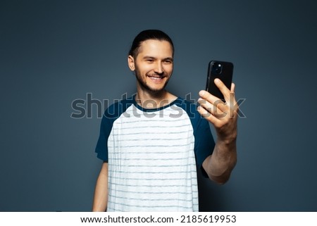 Studio portrait of young smiling man, taking selfie with smartphone.