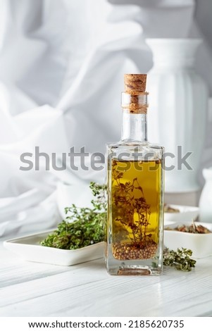 Olive oil with thyme and spices on a white wooden table.