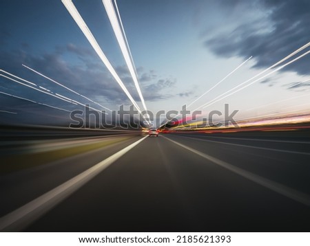 Speedy road drive along the evening highway. Front view from the car window to the road and other vehicles with beautiful light trails. Royalty-Free Stock Photo #2185621393