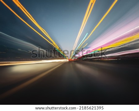 Beautiful image of a speedy night drive along the highway. Front view from the car window to the road, other vehicles and colorful light trails.