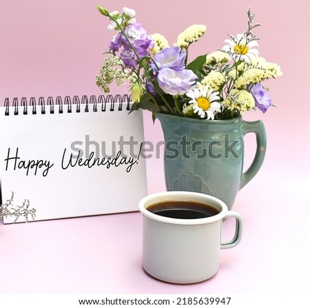 Happy Wednesday sign handwriting on notebook with cup of coffee and vase of flowers. Pastel pink.