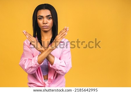 Close up portrait of serious young african american woman showing stop gesture with palm isolated on yellow background.