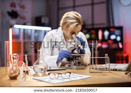 Young female researcher looking at the microscope in the life science, forensics, microbiology, biochemistry, genetics, oncology, laboratory.