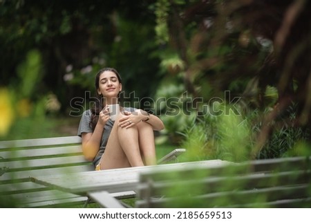 Cheerful and beautiful young carefree woman relaxing and breathing fresh air while sitting in balcony with nature view and drinking morning coffee and beverage and looking at scenic view Royalty-Free Stock Photo #2185659513