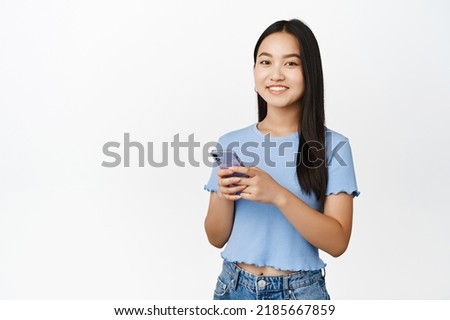 Cellular technology. Smiling asian girl holding smartphone and looking happy at camera, using mobile application, white background
