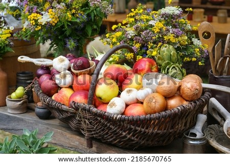 Basket full of apples, onions, garlic and artichokes, harvest from the vegetable garden decorated with bouquets of wildflowers on a rustic wooden table, selected focus, narrow depth of field