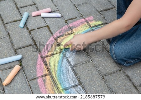 Portrait of a child drawing a rainbow on the street with colored chalk. Selective focus. Kid. A child is playing outside.
