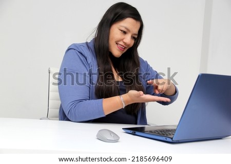 Latino adult woman speaks Mexican sign language with a deaf person through a laptop in a video call
