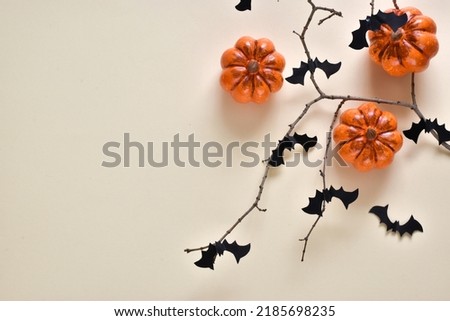Halloween holiday composition. Halloween decorations, pumpkins and bats on bare branch on light yellow background. Halloween party greeting card mockup. Copy space. Flat lay, top view