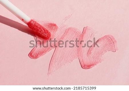 Smears of shining lip gloss and lip gloss brush on pink background, hard shadows