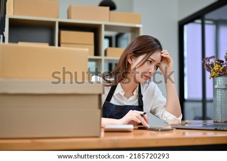 Attractive young Asian female entrepreneur or e-commerce business startup in the office perplexed by her online store website.
