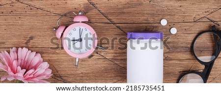 women health,middle age and menopause concept. health care style. copy space.white plastic bottle with pills, flowers, clock on wood background.banner
