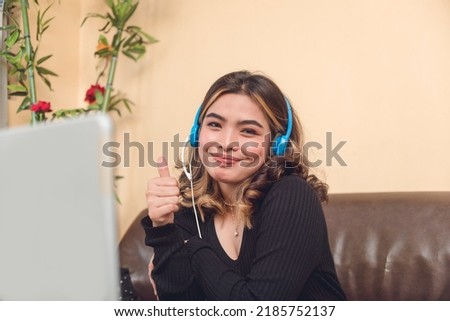 A portrait of a vlogger showing a thumbs up sign to show approval. She is wearing a blue wired headset.