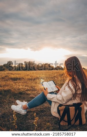 Christian woman holds bible in her hands. Reading the Holy Bible in a field during beautiful sunset. Concept for faith, spirituality and religion. Peace, hope Royalty-Free Stock Photo #2185758017