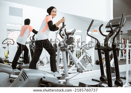 smiling beautiful women at the gym doing exercises on static elliptical cycle machine