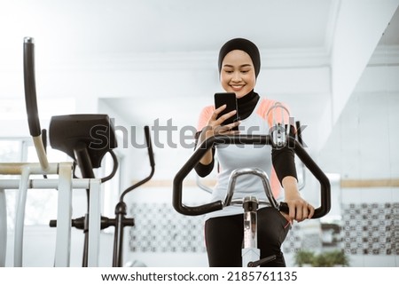 attractive muslim woman using mobile phone during exercising with static bike at the gym