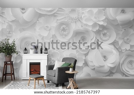 Interior of light living room with fireplace, armchair and table near wall with print of paper flowers