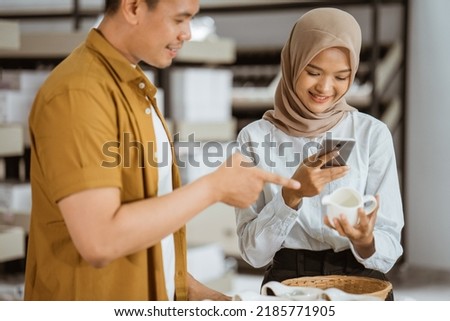 Veiled young woman using mobile phone camera to photograph cup in glassware shop