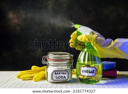 Using baking soda Sodium bicarbonate and white vinegar for home cleaning. White vinegar in spray bottle and baking soda in glass jar. Person spraying mist from bottle. Royalty-Free Stock Photo #2185774327