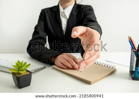 Business woman stretches out her hand while sitting at the desk in the office.