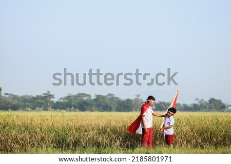 Two Asian school boy wearing uniform standing in the midst of the rice field and holding flag. Patriotic nationalism concept.