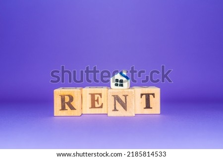 Wooden cubes with word RENT with miniature toy house on a purple,veri peri background.