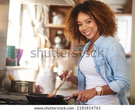 Whipping up something delicious just for you. Portrait of a happy young woman preparing a meal on the stove at home. Royalty-Free Stock Photo #2185814765
