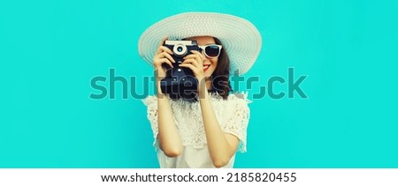Summer portrait of happy young woman photographer with film camera wearing white straw hat on blue background