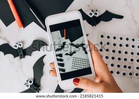 Taking photo on mobile phone of handmade Paper bats. Halloween holiday decorations. Happy Halloween party concept. Children's art project. DIY concept. Step by step Craft idea