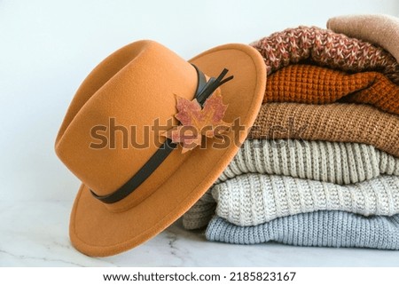 Stack of cozy knitted warm sweater with Autumn fall maple leaf and beige stylish hat. Sweaters in retro Style. Orange and blue colors. Cozy hygge concept Copy space Autumn season Royalty-Free Stock Photo #2185823167