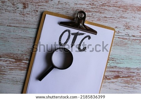 Top view image of paper clipboard with text OTC or Over The Counter and magnifying glass Royalty-Free Stock Photo #2185836399