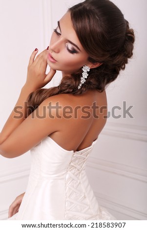 fashion photo of beautiful elegant bride with dark hair in wedding dress posing at studio