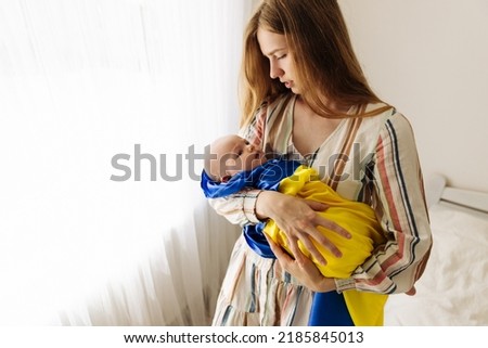 woman holds her sleeping little child in her arms, wrapped in a yellow and blue flag of Ukraine. protests against the war, shows patriotism and love for Ukraine. Independence Day