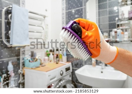 Close-up view of man's hand in a rubber protective glove with the plastic brush and the bathroom on the background. Cleaning concept.