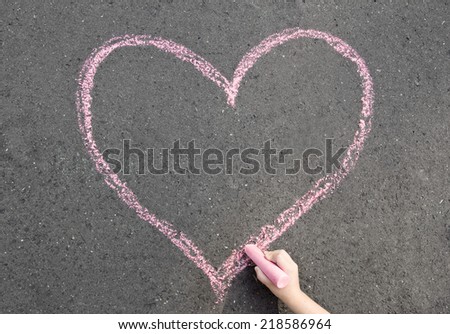 child hand drawing heart on the street