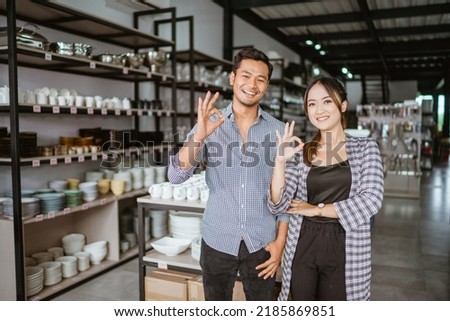 Asian man and woman standing with okay hand gesture at home appliance store